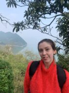 Mea stands in a red sweater with a scenic nature view in the background