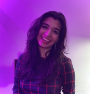 Cameron is smiling and surrounded by purple lighting. She is wearing a red striped dress.