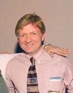 Man in a pink shirt behind a tan background