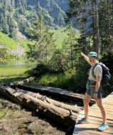 Woman on a dock in the forest pointing off into the trees and mountains