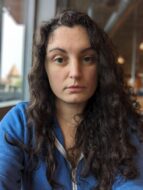 Woman with curly brown hair and a blue jacket.